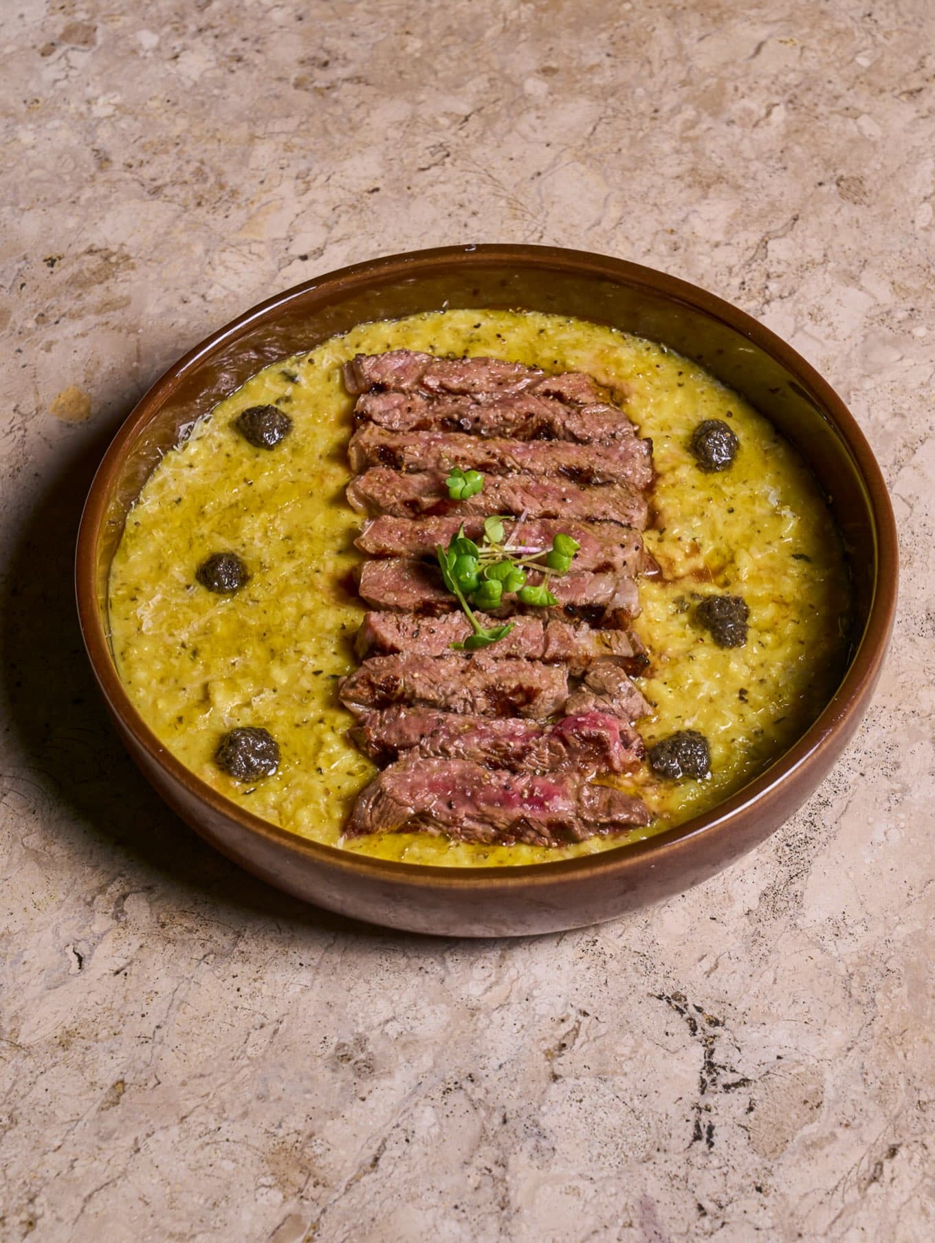 Risoto de açafrão com trufas negras e fatias de entrecot, em prato fundo, visto de cima