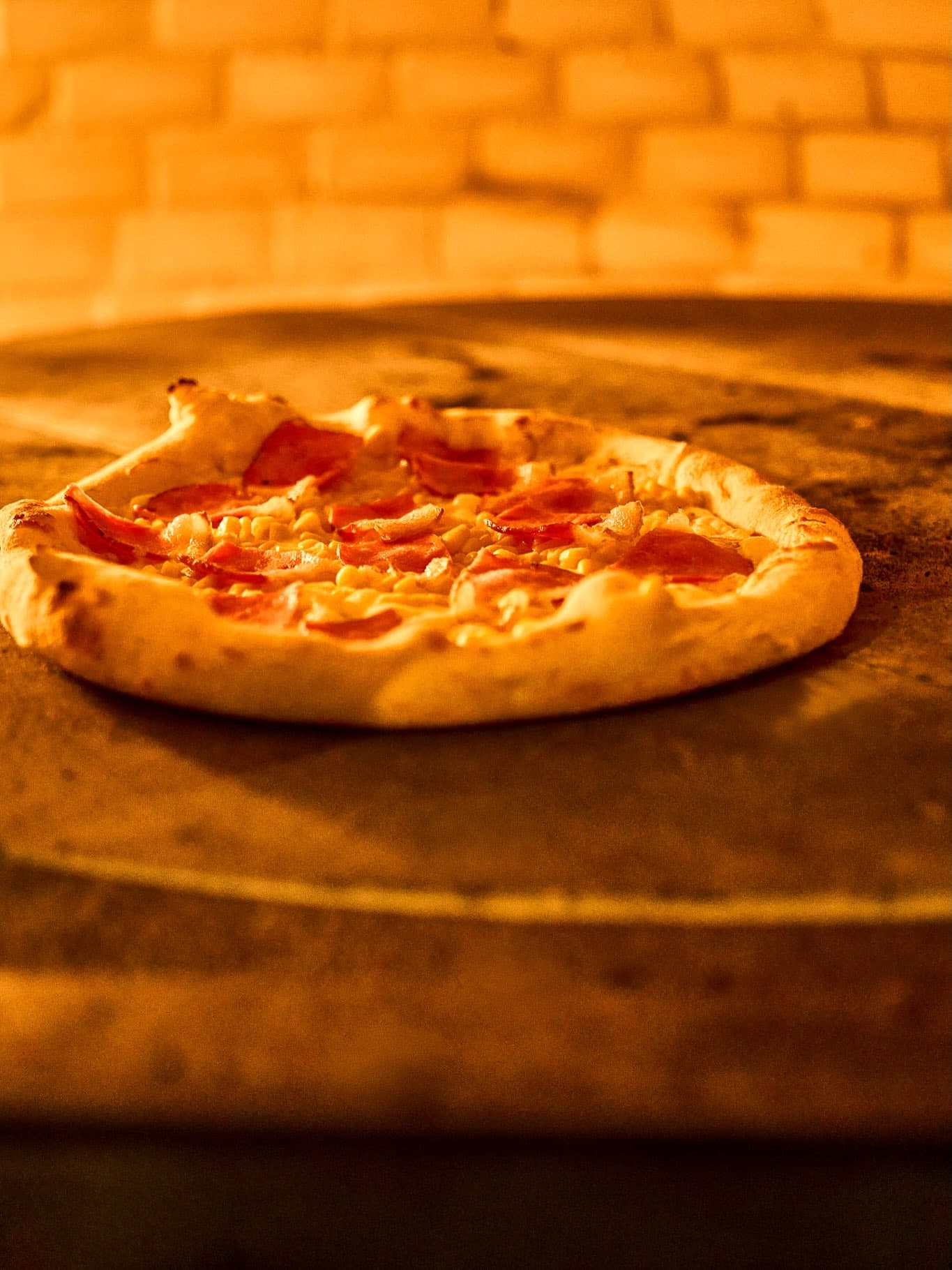 Pizza assando na boca do forno, sob a luz alaranjada do fogo