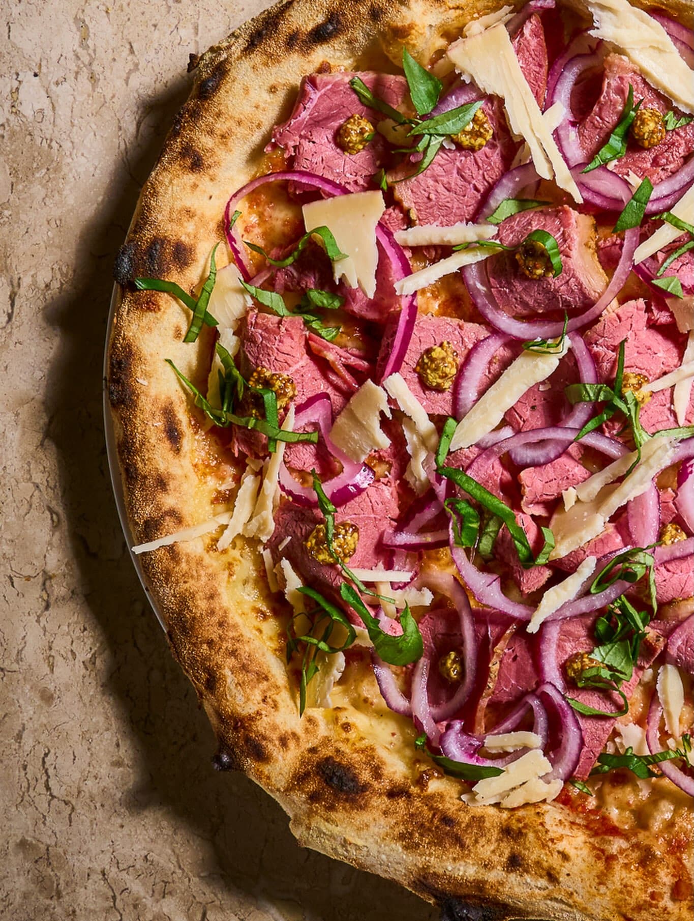 Pizza Pastrami & Dijon, com pastrami, cebola roxa, pickles de mostarda e lascas de queijo Tulia